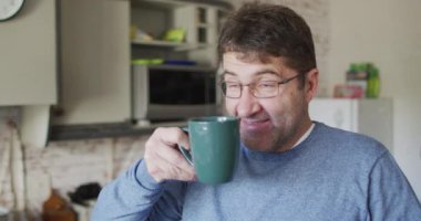 Gülümseyen ve gevşemiş beyaz adam evde mutfakta kahve içiyor. ev hayatı ve boş zaman kavramı.