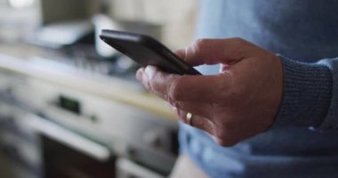 Evdeki mutfakta akıllı telefon kullanan beyaz adamın ellerini kapatıyoruz. ev hayatı ve boş zaman kavramı.