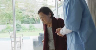 Gülümseyen Asyalı kadın doktor yaşlı kadın hastaya baston kullanarak yürümesine yardım ediyor. üst düzey sağlık ve sağlık hizmetleri.