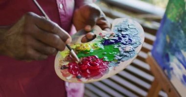 Afrika kökenli Amerikalı son sınıf öğrencisinin boya paleti kullanarak tuvale resim çizmesi. Emeklilik hayatı, evde yalnız zaman geçirmek..