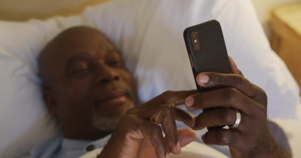 Szczęśliwy Afrykański Starszy Mężczyzna Leżący Łóżku Korzystający Smartfona Uśmiechnięty Styl — Wideo stockowe