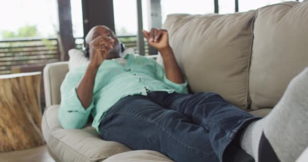 Счастливый Афроамериканец Старший Мужчина Расслабляется Лежит Диване Наушниках Слушает Музыку — стоковое видео
