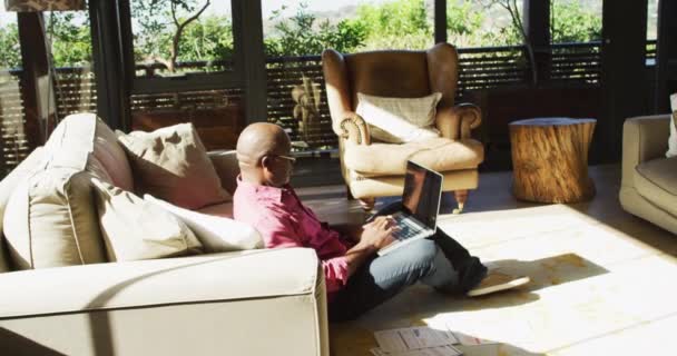 アフリカ系アメリカ人のシニア男性は 太陽の下でノートパソコンを使用して作業のリビングルームの床に座っている 家で一人で過ごす退職生活や — ストック動画