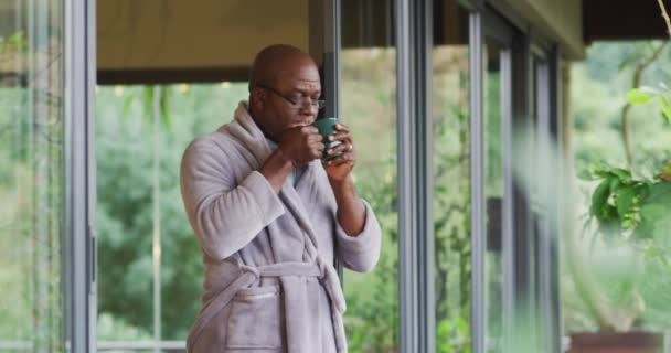 非裔美国老人穿着浴衣站在阳台上喝咖啡 欣赏风景 退休生活方式 独自呆在家里 — 图库视频影像