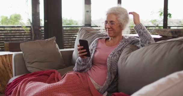 高级混血女子坐在沙发上使用智能手机 退休和老年生活方式 独自呆在家里 — 图库视频影像