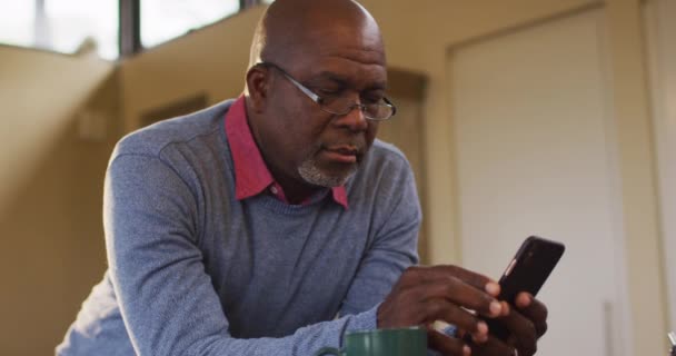 Hombre Mayor Afroamericano Apoyado Mostrador Cocina Usando Teléfono Inteligente Quitándose — Vídeo de stock