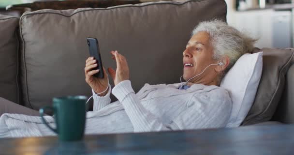 Senior Gemengde Ras Vrouw Liggend Bank Het Dragen Van Oortelefoons — Stockvideo