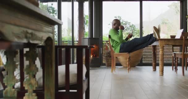 아프리카 미국인 식탁에 편안하게 스마트폰을 사용하고 있습니다 집에서 시간을 보내는 — 비디오