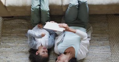 Melez anne ve kızın yerde yatıp eğleniyor ve tablet kullanıyor. ev hayatı ve aile eğlence zamanı konsepti.