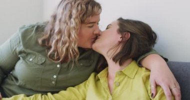 Kafkasyalı lezbiyen çift kanepede öpüşüyor ve oturuyor. Ev hayatı, evde dinlenerek boş zaman geçirmek..