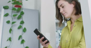 Beyaz kadın sarı gömlek giyiyor ve akıllı telefon kullanıyor. Ev hayatı, evde dinlenerek boş zaman geçirmek..