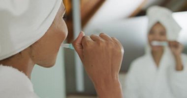 Karışık ırktan bir kadın ayna fırçalayan dişlere bakıyor. ev hayatı, kaliteli boş zaman geçirmek evde dinlenmek..