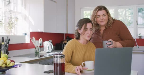 幸せな白人レズビアンコーヒーを飲み キッチンでラップトップを使用しています 国内生活と余暇 — ストック動画
