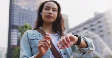 Asyalı kadın kulaklık takıyor ve akıllı kaset kullanıyor. Dijital göçebe şehirde geziyor, dolaşıyor..