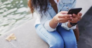 Fıskiyenin yanında oturan Asyalı kadın akıllı telefon kullanıyor. Dijital göçebe şehirde geziyor, dolaşıyor..