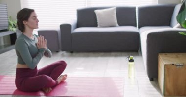 Beyaz kadın formda ve yoga minderinde meditasyon yapıyor. Ev hayatı, evde dinlenerek boş zaman geçirmek..