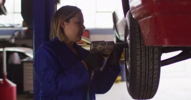 Kadın tamirci, araba servis istasyonunda elektrikli matkap kullanarak arabanın lastiklerini değiştiriyor. otomobil tamir servisi