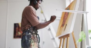 Sanat stüdyosundaki tuvale kulaklık takan Afrikalı Amerikalı erkek sanatçı. sanat, hobi ve yaratıcı meslek kavramı