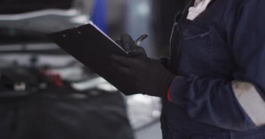 Kadın tamircinin orta bölümü bir araba servis istasyonundaki panoya not alıyor. otomobil tamir servisi