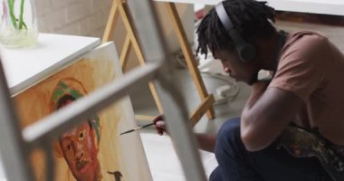Sanat stüdyosundaki tuvale kulaklık takan Afrikalı Amerikalı erkek sanatçı. sanat, hobi ve yaratıcı meslek kavramı