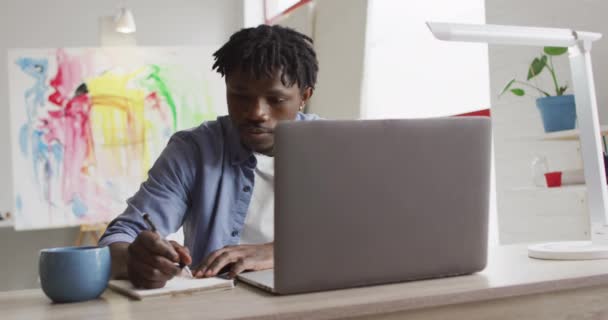 Αφροαμερικάνος Καλλιτέχνης Φορητό Υπολογιστή Που Κρατάει Σημειώσεις Ενώ Κάθεται Στο — Αρχείο Βίντεο