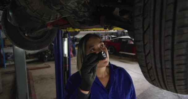 トーチライトを使用し 車のサービスステーションで車の下で働く女性の整備士 自動車修理サービス — ストック動画