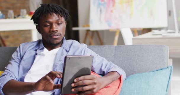 非洲裔美国男性艺术家坐在艺术工作室的沙发上 微笑着使用数码平板电脑 业余爱好和创造性职业概念 — 图库视频影像