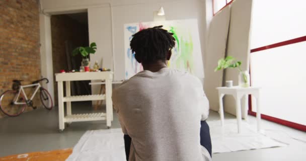 Rückansicht eines nachdenklichen afrikanisch-amerikanischen Künstlers, der im Kunstatelier vor seinem Gemälde sitzt. Kunst, Hobby und kreatives Beschäftigungskonzept