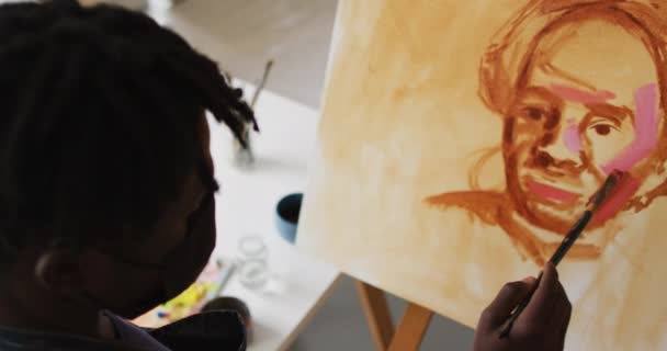 アフリカ系アメリカ人の男性アーティストは アートスタジオでキャンバスにフェイスマスク絵を着ています コロナウイルスCovid 19パンデミック時のアートスタジオでの衛生状態 — ストック動画