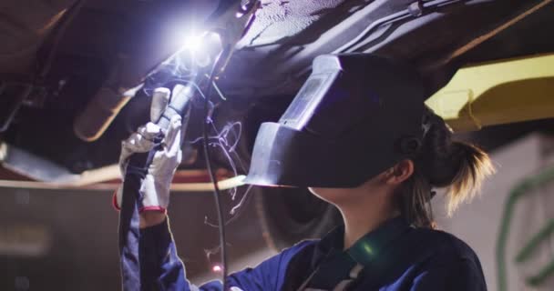 Γυναίκα Μηχανικός Φορώντας Συγκόλληση Κράνος Συγκόλλησης Κάτω Από Ένα Αυτοκίνητο — Αρχείο Βίντεο