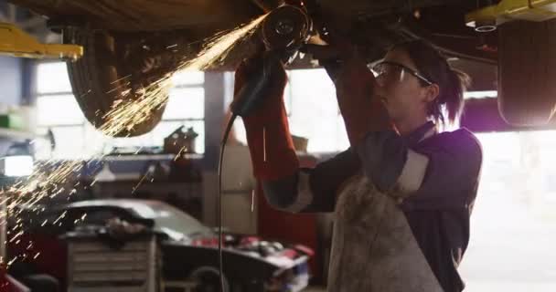 Mechanikerin Mit Einem Elektrischen Messerschneider Und Arbeitet Unter Einem Auto — Stockvideo