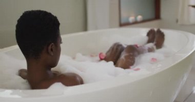 Afro-Amerikan çekici bir kadının köpük ve gül yapraklarıyla banyo yapması. güzellik, şımartma, spa ve refah konsepti.