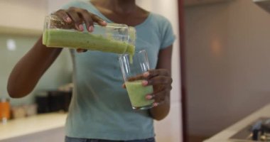 Afro-Amerikan çekici kadının elleri mutfakta ev yapımı smoothie 'yi cama döküyor. evde sağlıklı beslenme ve yaşam tarzı.