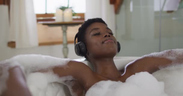 Mosolygó Afro Amerikai Vonzó Fejhallgatót Visel Pihentető Hab Fürdő Fürdőszobában — Stock videók