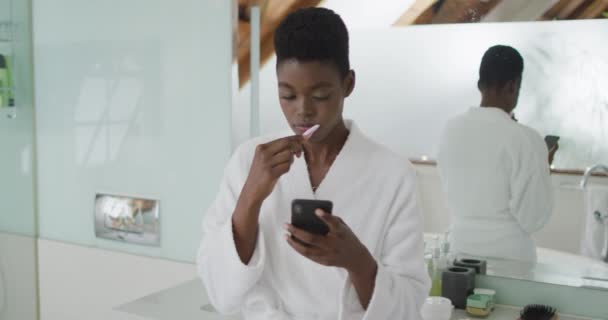 Mujer Afroamericana Atractiva Cepillarse Los Dientes Uso Teléfono Inteligente Baño — Vídeos de Stock