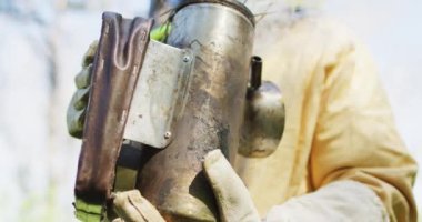 Beyaz erkek arı yetiştiricisi koruyucu giysiler içinde sigara hazırlıyor. Arı ve bal üretimi, küçük tarım işi ve hobi.