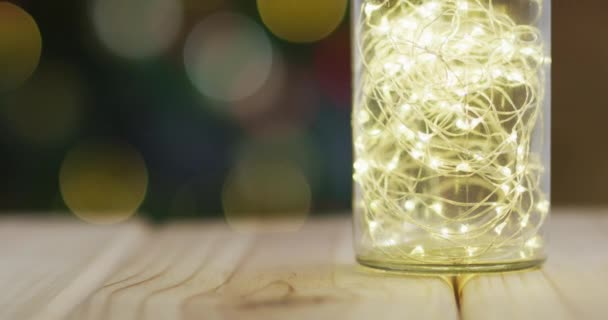 クリスマスツリーの上に瓶の中に妖精の光と木製のテーブルのビデオ クリスマス お祝いのコンセプト — ストック動画