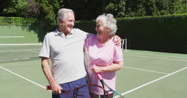 快乐的资深高加索夫妇手握网球拍 拥抱在网球场上 退休及运动 — 图库视频影像