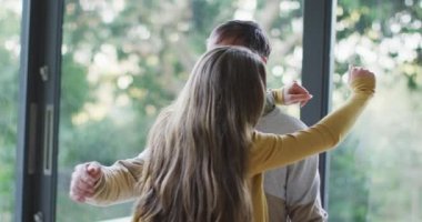 Mutlu Kafkasyalı baba ve genç kız bahçe manzaralı pencerenin önünde kucaklaşıyorlar. Aile evde vakit geçiriyor..