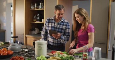 Gülümseyen Kafkas babası ve ergen kızı mutfakta tablet kullanarak sağlık içeceği hazırlıyorlar. Aile evde vakit geçiriyor..