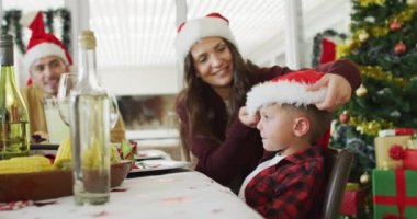 Mutlu Kafkasyalı anne noel masasında oğluna Noel Baba şapkası takıyor. Aile Noel 'i ve şenliği evde birlikte kutluyoruz..