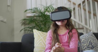 Kafkasyalı kız vr kulaklık takıyor, kanepede oturuyor ve eğleniyor. çocukluk, eğlence ve keşif teknolojiyi evde kullanmak.