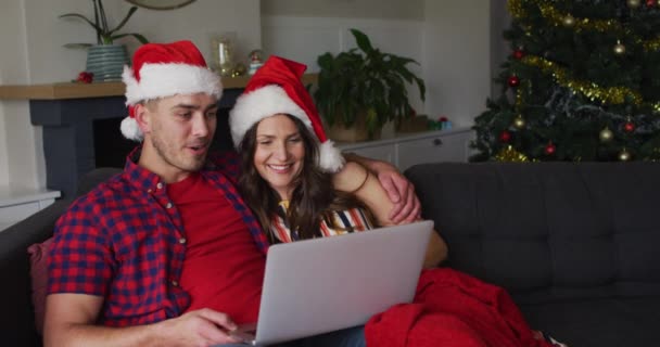 Feliz Casal Caucasiano Vestindo Chapéus Papai Noel Sentado Sofá Usando — Vídeo de Stock