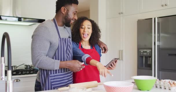 幸せなアフリカ系アメリカ人のカップル 一緒にタブレットやベーキングを使用してエプロンを身に着けている 家族で楽しみながら — ストック動画