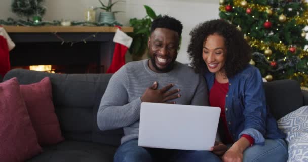 アフリカ系アメリカ人のカップルがビデオ通話とジェスチャー バックグラウンドでクリスマスの装飾を持って笑顔 クリスマスの時間と祭りを一緒に家で — ストック動画