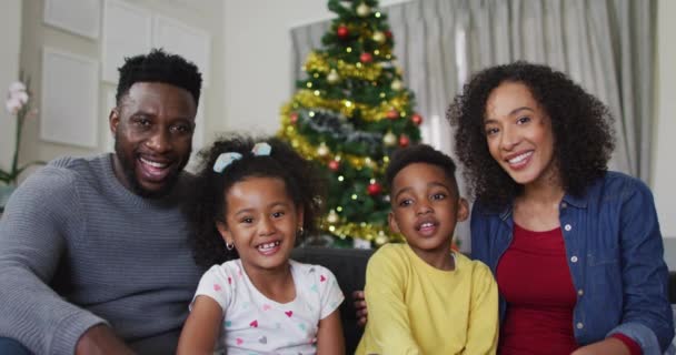 ビデオ通話とジェスチャー バックグラウンドでクリスマスの装飾を持っているアフリカ系アメリカ人の家族を笑顔 クリスマスの時間と祭りを一緒に家で — ストック動画