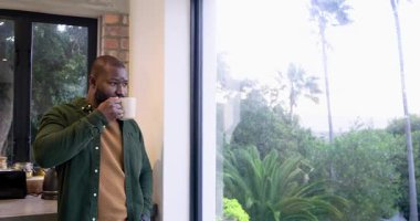 Açık renkli Afro-Amerikan bir adamı kupayla pencereye çekiyor, bahçeyi yudumluyor ve derin derin düşünüyor, kopya uzayı. Düşünce, huzur, farkındalık, ev, konfor, doğal yaşam tarzı