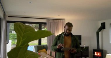 Afro-Amerikalı bir adam yemek masasında bir sonraki adımı düşünürken tableti tıkırdatıyor ve aşırıyor. Teknoloji, yaşam tarzı, modern, rahatlama, ev, yenilik, eğlence