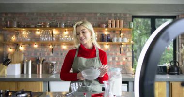 Yüzük ışığı ve telefonla çekim yapan bir kadın mutfakta un süzerek yemek tarifi sunuyor. Pişirme, pişirme, aşçılık, yemek hazırlama, ev stüdyosu, yaşam tarzı, kırsal