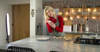 Kadın halka hafif akıllı telefonuna danışmanlık yapıyor, özel ders için mutfak adasındaki kurabiyelere boru hattı dizayn ediyor. Pişirme, aşçılık, modern, yerli, sanatçılık, işçilik, yaşam tarzı